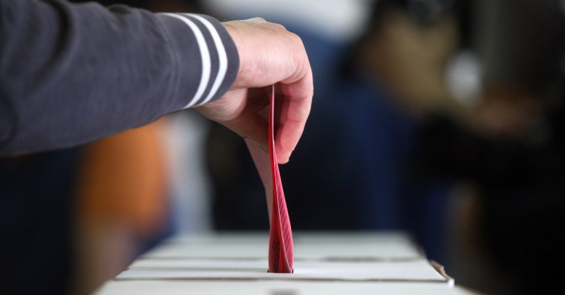 Eldre mann som stemmer ved valg, hånd legger stemmeseddelen i valgurnen.